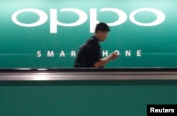 A commuter using his mobile phone passes an advertisement of Chinese smartphone maker Oppo at a train station in Singapore, May 8, 2014.