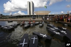 Indigenous protesters from various ethnic groups place fake coffins, representing Indians killed over the demarcation of land, in a reflecting pool outside the National Congress as they demand the demarcation of indigenous lands in Brasilia, Brazil, April 25, 2017.
