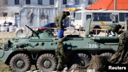 Sejumlah orang bersenjata dengan kendaraan lapis baja, diyakini dari Rusia, terlihat di depan markas angkatan laut Ukraina di Pelabuhan Krimea di Kota Feodosia (23/3).