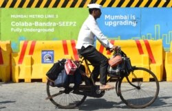 Seorang "dabbawala" atau kurir pembawa makanan, bersepeda melewati lokasi kerja kereta api metro di Mumbai, 14 Desember 2017. (AFP)