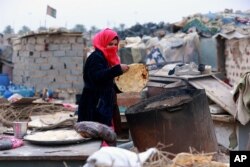 Umm Salem bakes bread in front of her hut at an encampment for the displaced outside Baghdad, Iraq, Feb. 12, 2018.