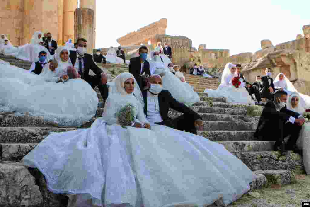 Lebanese couples, wearing protective face masks, sit on the steps during a group wedding at the Temple of Bacchus at the historic site of Baalbek in Lebanon&#39;s eastern Bekaa Valley.