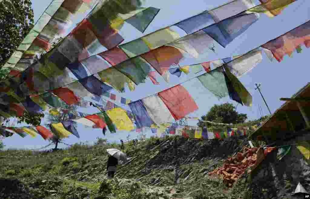 A Buddhist walks under prayer flags after paying her respects to those who died in the recent earthquake, at the Nedyon Unphong Thapchyo Monastery in Bidur, Nuwakot District, Nepal, May 4, 2015. 
