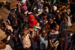 Seorang perempuan terlihat menggendong bayinya di antara pengungsi dan migran dari kamp Moria yang melancarkan aksi protes dekat Mytilene di pulau Lesbos, Yunani, 12 September 2020. (Foto: dok).