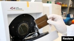 FILE - A biotechnician demonstrates the loading of a genome sequencing machine at the J. Craig Venter Institute in Rockville, Maryland. Relative to their ability to pay, cancer patients in China and India face much higher prices than wealthier U.S. patients.