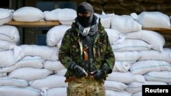 An armed man, who is wearing black and orange ribbons of St. George - a symbol widely associated with pro-Russian protests in Ukraine, stands guard in front of barricades outside the mayor's office in Slovyansk April 18, 2014. 