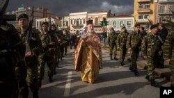 An Orthodox priest holds a cross as he is accompanied by a guard of honor during an Epiphany ceremony to bless the water in Mytilene port on the northeastern Greek island of Lesbos, Jan. 6, 2016.