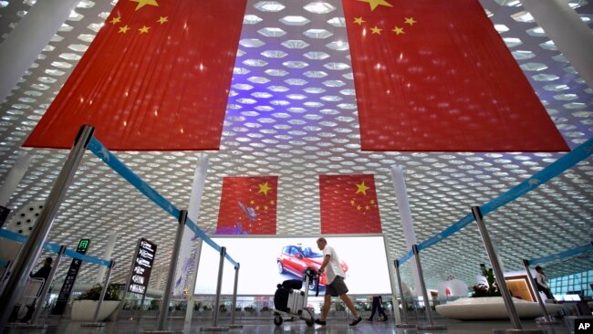 资料照：一名旅客推着行李车从深圳机场悬挂的中国国旗下走过。