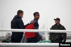 An officer (L) from European Union border agency Frontex escorts a migrant boarding a Turkish-flagged passenger boat, to be returned to Turkey, on the Greek island of Lesbos, April 8, 2016.