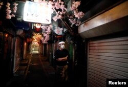 日本政府宣布紧急状态后，东京新宿区一家餐馆的服务生站在空荡无人的小巷里。（2020年4月8日）