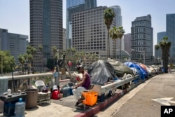 FILE - A homeless man sits at his street-side tent along Interstate 110 along downtown Los Angeles' skyline, May 10, 2018. Thousands of homeless people sleep on the streets of Los Angeles County.