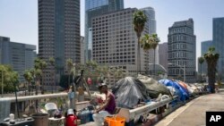 FILE - A homeless man sits at his street-side tent along Interstate 110 in downtown Los Angeles, May 10, 2018.