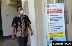 Seorang staf UGM melintas di depan poster terkait Virus Corona di kampus tersebut. (Foto:VOA/ Nurhadi)