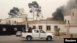 Armed men aim their weapons from a vehicle as smoke rises in the background near the Libyan parliament building in Tripoli May 18, 2014.