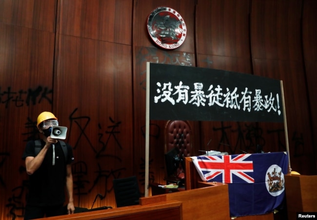 一名进入香港立法会的抗议者站在挂在立法会内的香港殖民地旗帜旁使用扩音喇叭讲话。（2019年7月1日）