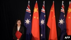 Seorang petugas berdiri di samping bendera nasional China dan Australia sambil memegang salinan perjanjian perdagangan bebas (FTA) saat berlangsungnya penandatanganan kesepakatan di Canberra, Australia, 17 Juni 2015. (Foto: dok).