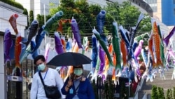 Personas con máscaras faciales para ayudar a detener la propagación del coronavirus caminan bajo coloridas serpentinas de peces en Tokio el sábado 2 de mayo de 2020. El primer ministro Shinzo Abe anunció que extenderá el estado de emergencia más allá del 6 de mayo porque las infecciones están aumentando y los hospitales están abrumados.