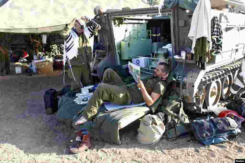 An Israeli soldier reads a newspaper as another one prepares to pray next to an armored personnel carrier near the southern Gaza Strip, July 17, 2014.