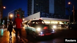 People wait on the sidewalk for transportation as a vintage U.S. car used as private taxi passes by in Havana, Cuba, Sept. 20, 2018.