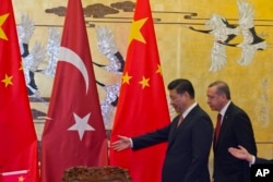 FILE - Chinese President Xi Jinping, left, shows the way for Turkey's President Recep Tayyip Erdogan as they attend a signing ceremony at the Great Hall of the People in Beijing, July 29, 2015.