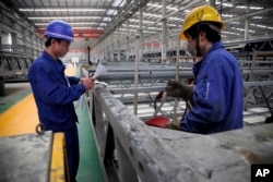 FILE - workers look over building beams at the Broad Sustainable Building Co. in Yueyang in central China's Hunan Province.