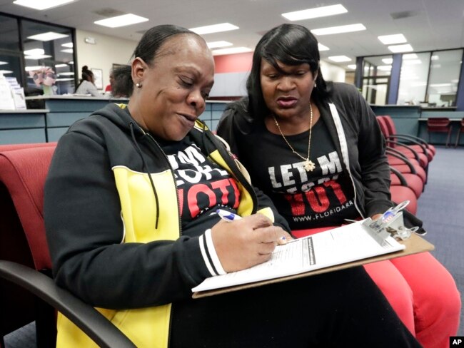 Former felon Yolanda Wilcox, left, fills out a voter registration form as her best friend Gale Buswell looks on at the Supervisor of Elections office, Jan. 8, 2019, in Orlando.