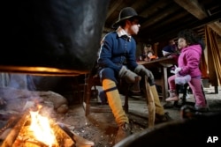 In this Sunday, Nov. 18, 2018, photo, actor David Madden, of Carver, Mass., left, in the role of Pilgrim John Cooke, interacts with visitors at Plimoth Plantation living history museum village, in Plymouth, Mass. (AP Photo/Steven Senne)