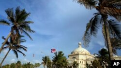 In this July 29, 2015, file photo, U.S. and Puerto Rican flags fly in front of Puerto Rico’s Capitol as in San Juan, Puerto Rico. 