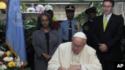 With Achim Steiner, executive director of the U.N. Environment Program, right, looking on, Pope Francis signs the visitors book at the United Nations regional office in Nairobi, Kenya, Nov. 26, 2015.