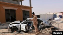 Seorang laskar Libya yang tergabung dalam faksi aliansi pemerintah Tripoli berdiri dekat kendaraan yang rusak akibat serangan udara di Ben Jawad, 2 Februari 2015. (Foto: dok.)