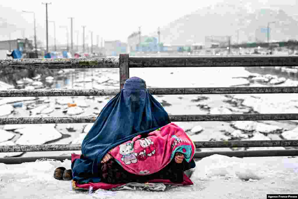 A burqa-clad Afghan woman sits with a child on her lap as she seeks alms from passers-by on a bridge covered with snow in Kabul.