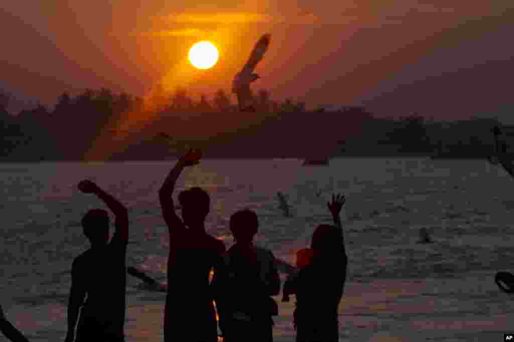 A group of people wave as seagulls fly near by during the last sun set of the year at a jetty in Yangon river, Myanmar, Dec.31, 2014.