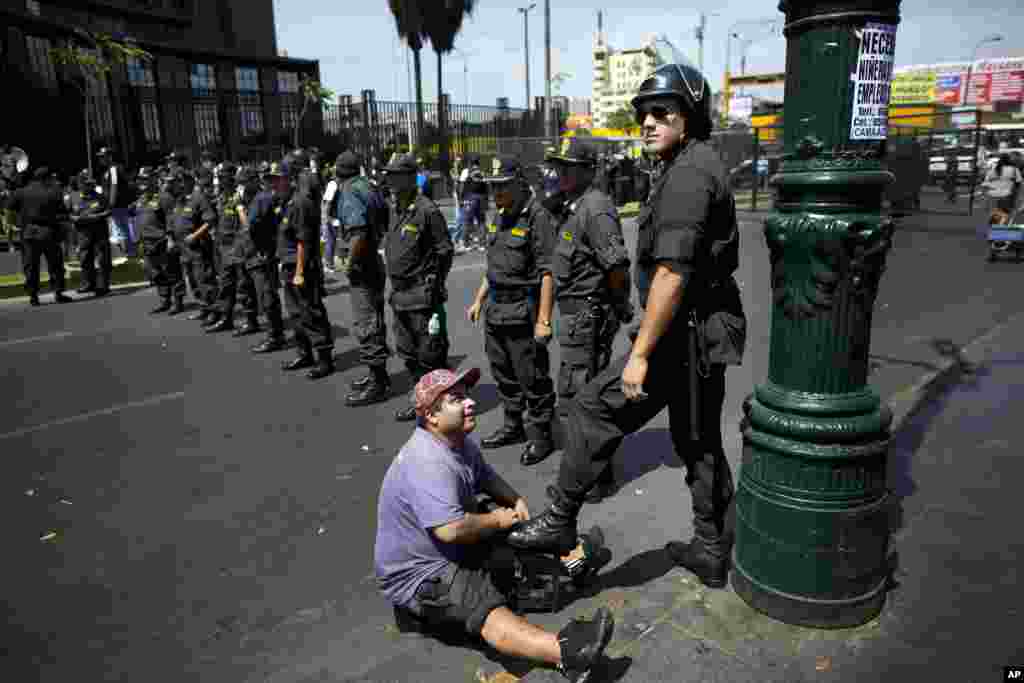 A shoe-shiner polishes the boots of a policeman who is standing guard during a protest organized by artisanal and small-scale gold miners in Lima, Peru, Mar. 24, 2014.