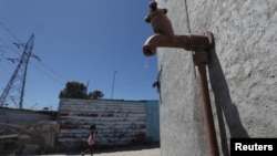 FILE - Residents walk past a leaking communal tap in Khayelitsha township, near Cape Town, South Africa, Dec. 12, 2017.