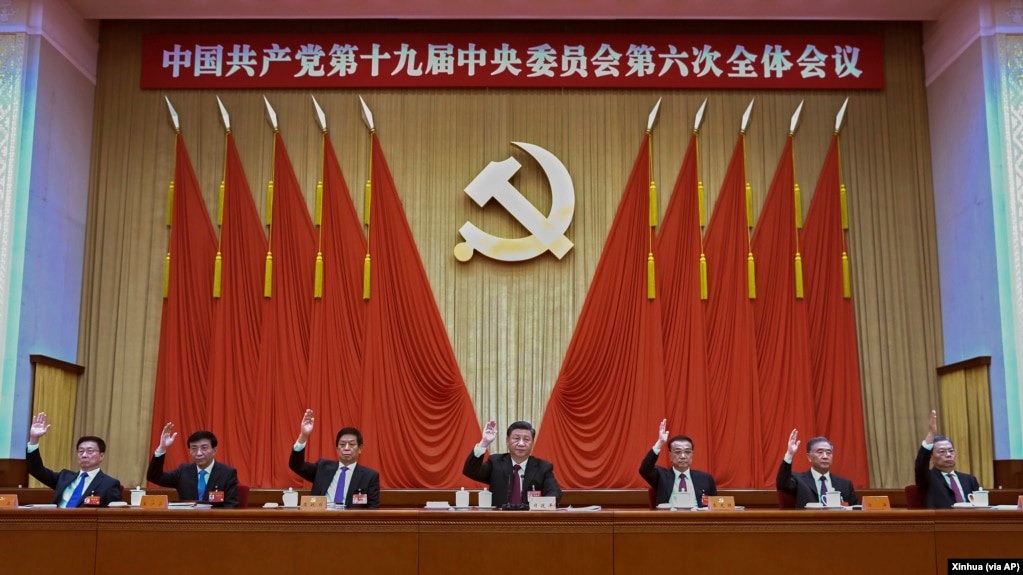 在新华社发布的这张照片中，包括中国国家主席习近平（中）和国务院总理李克强（右三）在内的中共中央政治局常委在十九大会议上举手。(photo:VOA)