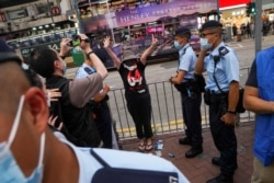 香港警察在维多利亚公园外拦截一名妇女，她身穿纪念六四的T恤，做出反送中运动“五大诉求 缺一不可”的手势。（2021年6月4日）