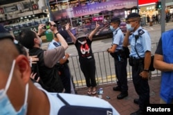 香港警察在维多利亚公园外拦截一名妇女，她身穿纪念六四的T恤，做出反送中运动“五大诉求 缺一不可”的手势。（2021年6月4日）
