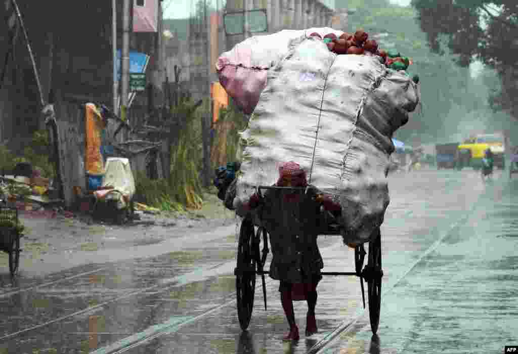 An Indian rickshaw-puller transports goods along a road in heavy rain in Kolkata.