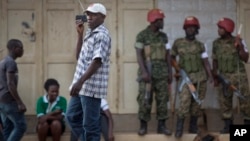 FILE - In this Saturday, Feb. 20, 2016 file photo, a man walks past listening to news on a portable radio as military police deploy, shortly after the election result was announced, and social media had been blocked, in downtown Kampala, Uganda. 