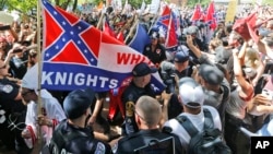 FILE- Members of the white supremacist KKK are escorted by police past a large group of protesters during a KKK rally in Charlottesville, Virginia, July 8, 2017.
