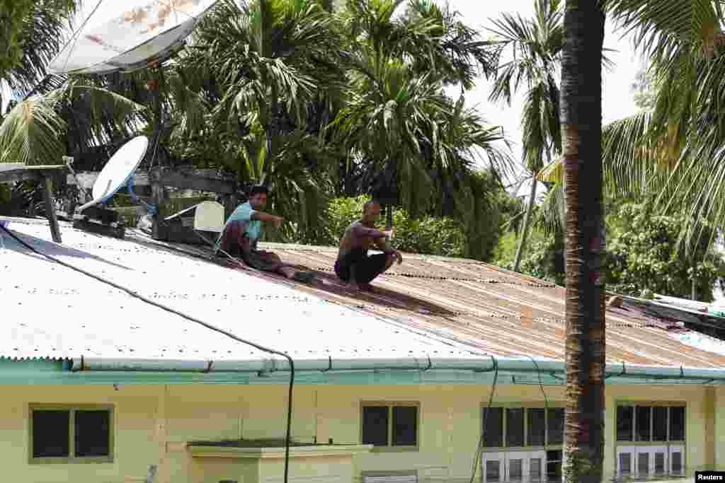 Men gesture on the roof of a home in a flooded village at Kalay township, Sagaing region, Aug. 2, 2015.