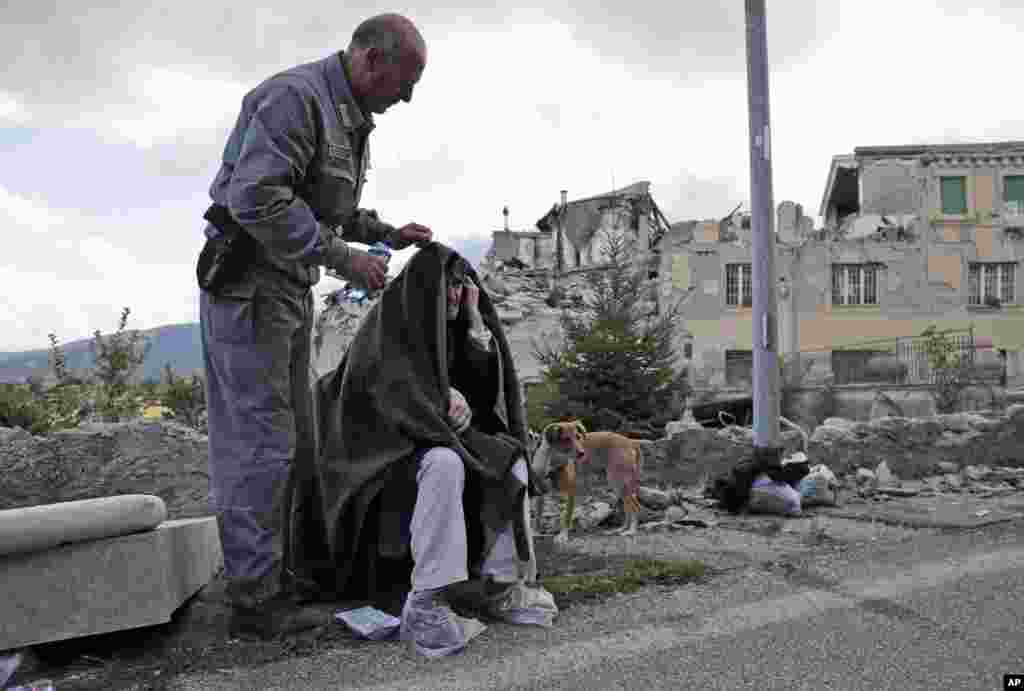 An elderly man is given assistance as collapsed buildings are seen in the background following an earthquake in Amatrice, Italy, Aug. 24, 2016.
