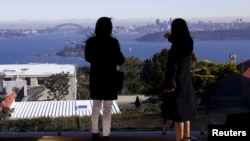 FILE - The Sydney Opera House and Harbour Bridge can be seen behind real estate agent LuLu Sun (R) as she escorts Bao Fang, a potential buyer from Shanghai, during an inspection of a property for sale in the Sydney suburb of Vaucluse, Australia, July 11, 