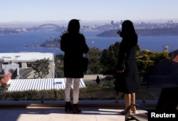 FILE - The Sydney Opera House and Harbour Bridge can be seen behind real estate agent LuLu Sun (R) as she escorts Bao Fang, a potential buyer from Shanghai, during an inspection of a property for sale in the Sydney suburb of Vaucluse, Australia, July 11,