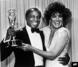 FILE - Actor Robert Guillaume, star of "Benson," gets a hug from Linda Gray of "Dallas" who presented him with the Emmy for outstanding lead actor in a comedy series, in Pasadena, Calif., Sept. 22, 1985.