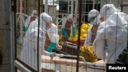 British health workers lift a newly admitted Ebola patient onto a wheeled stretcher in to the Kerry town Ebola treatment center outside Freetown, Sierra Leone, Dec. 22, 2014.