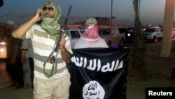 A fighter of the Islamic State of Iraq and the Levant (ISIL) holds a weapon while another holds a flag in the city of Mosul, June 23, 2014. 