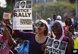 Female residents hold up images of black teenager Trayvon Martin and a packet of Skittles candy during a rally demanding justice for his killing in Miami, Florida April 1, 2012.