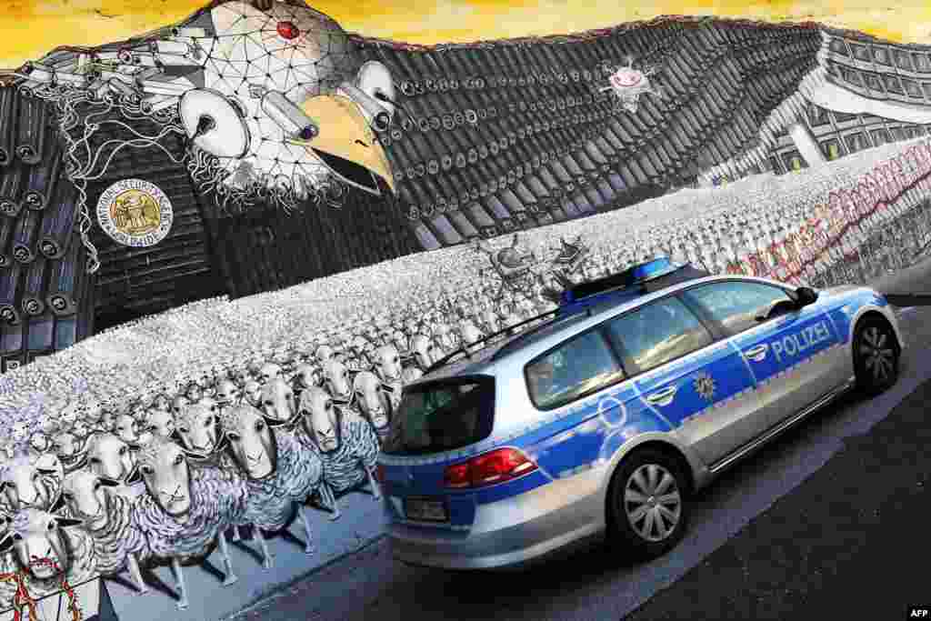 A German police car passes a mural painting featuring the emblematic U.S. eagle with a badge that reads "National Security Agency Worldwide" at the at the Ehrenfeld railway embankment in Cologne, western Germany.