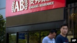 FILE - People walk past an entrance to the Anbang Insurance Group's offices in Beijing, June 14, 2017.